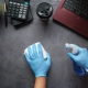 Hands wearing blue latex gloves and using cleaning supplies to clean a desk